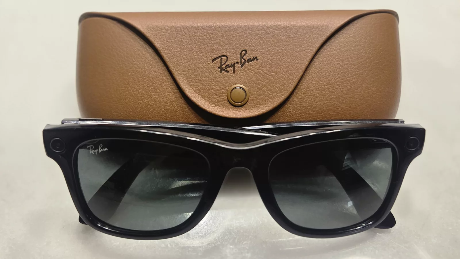 Ray-Ban Meta Gen 1 smart glasses with charging case.jpg. A pair of shiny black Ray-Ban Meta Gen 1 smart glasses positioned in front of their brown leather charging case.. Ilustracija uz vest: Meta Connect pokazao koliko kompanija ulaže u pametne naočare