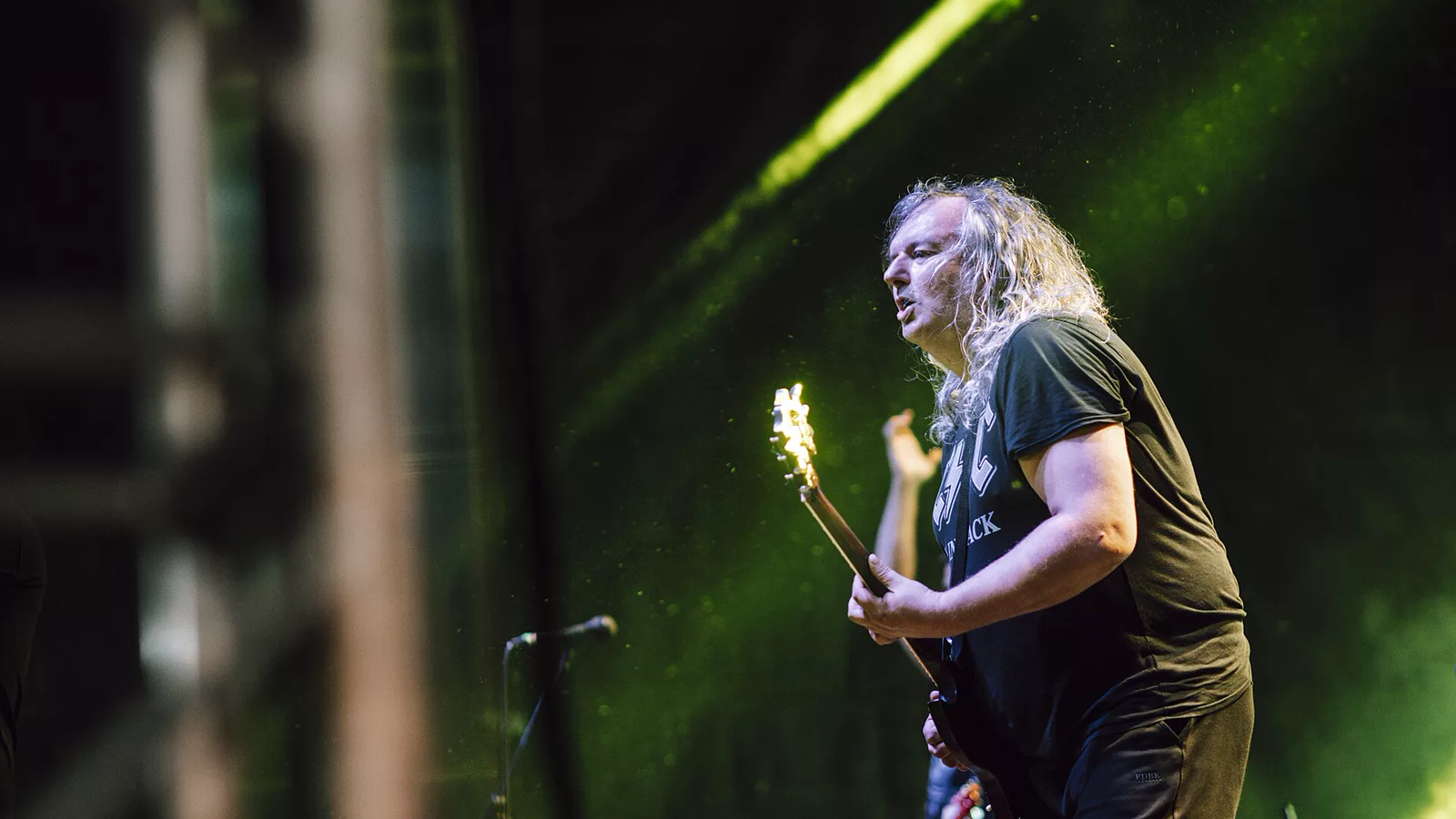 Guitarist performs energetically on stage during a vibrant music festival in the evening light.jpg. A skilled guitarist with long hair passionately plays his guitar on stage, captivating the audience under colorful lights during a lively music festival.. Ilustracija uz vest: Queens of the Stone Age objavili novu pesmu „Where The Goth Girls At?“